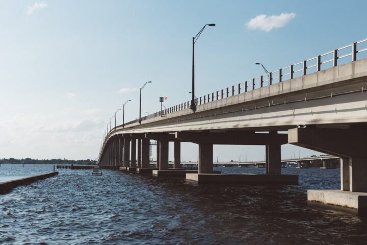 brown concrete bridge above body of water under blue sky and white clouds