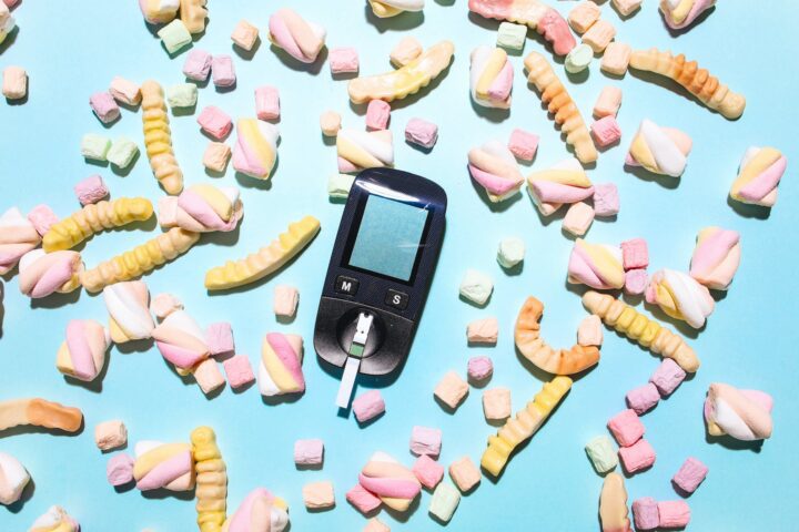 glucose meter surrounded by sweet treats on a blue surface