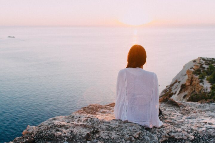 woman sitting on gray rock near body of water