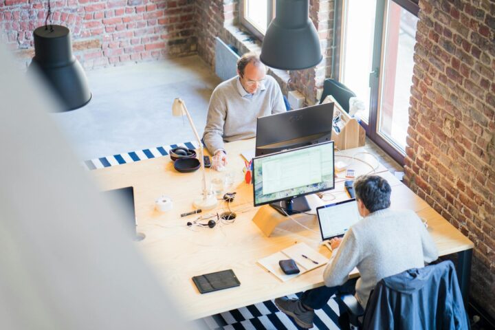 two men sitting facing on flat screen monitors