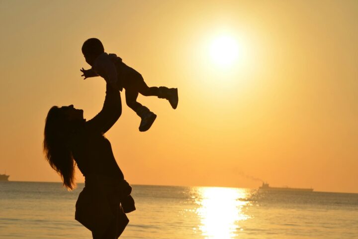 silhouette photo of a mother carrying her baby at beach during golden hour